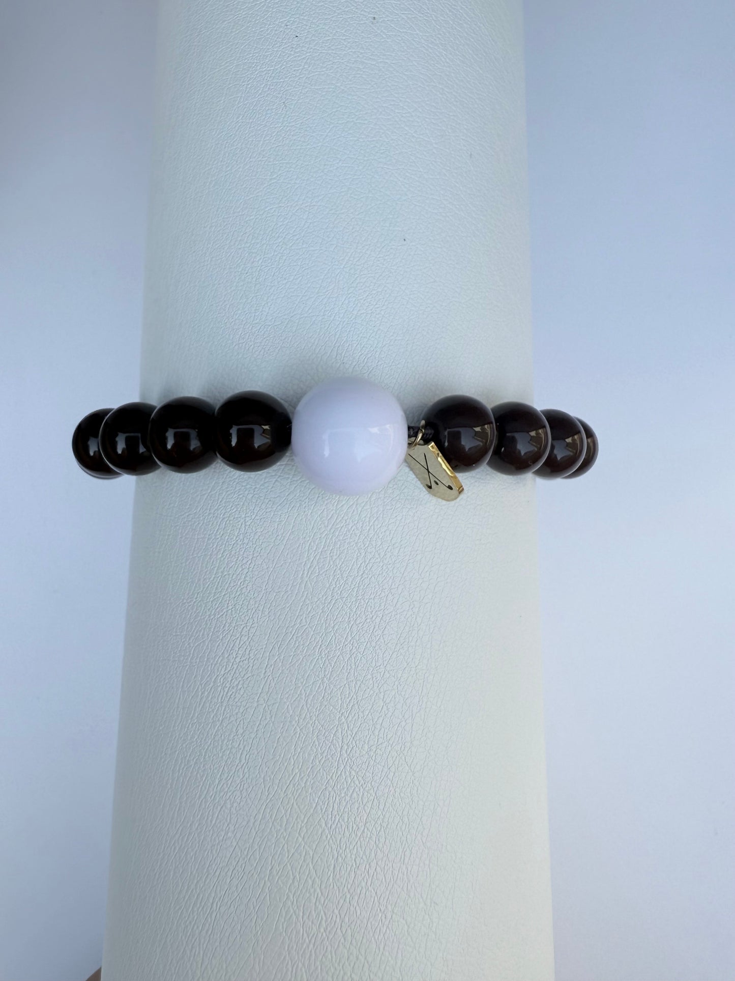 Bracelet with dark beads and a white bead on a white stand against a light gray background