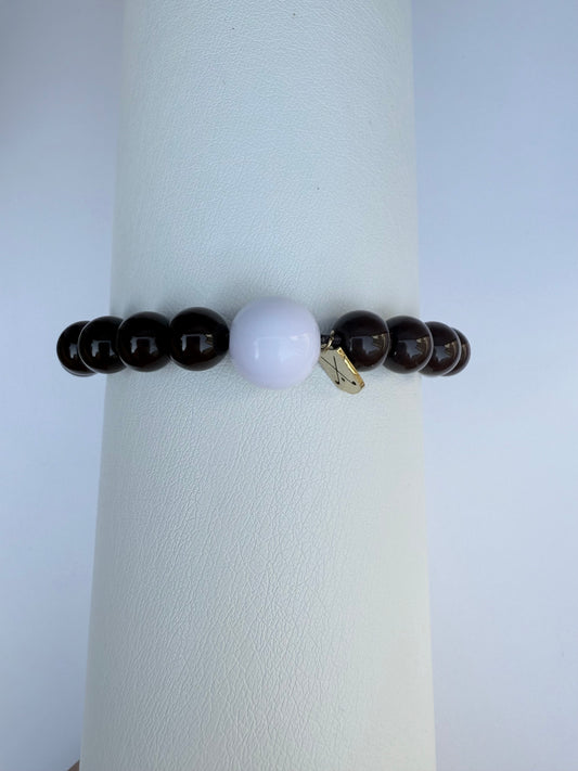 Bracelet with dark beads and a white bead on a white stand against a light gray background