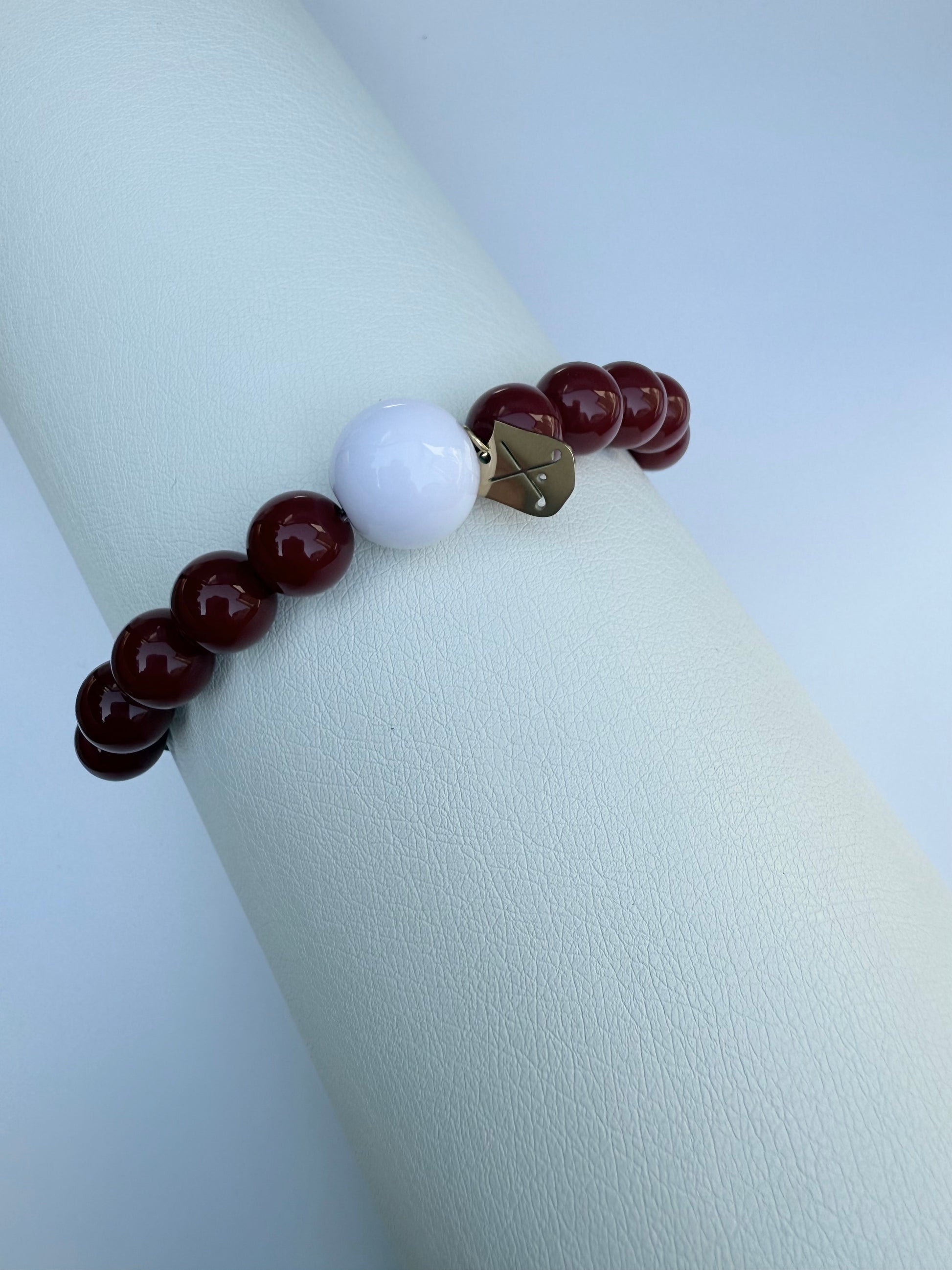 Bracelet with red beads and a white bead on a white surface
