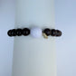 Bracelet with dark beads and a white bead on a white stand against a light gray background