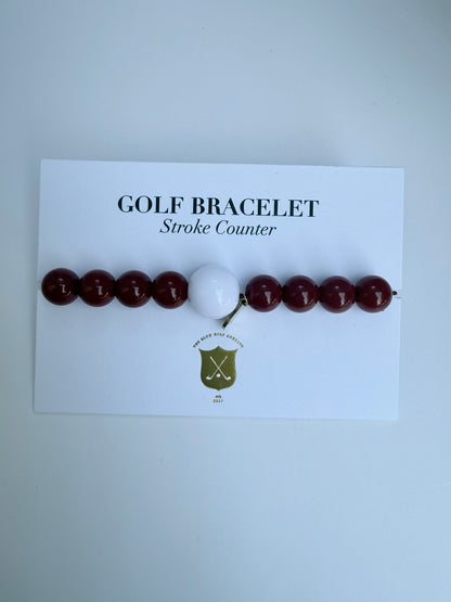 Golf bracelet with red beads and a white ball on a card labeled 'Golf Bracelet Stroke Counter' against a light gray background.